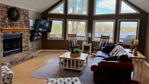 Un salón amplio con chimenea, ventanas grandes, televisor y asientos cómodos.