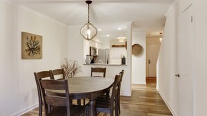 Un coin repas avec une table ronde en bois et des chaises, un luminaire suspendu et une cuisine en arrière-plan.