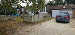 A residential driveway with a parked car, a wooden fence, and a house with a garage.