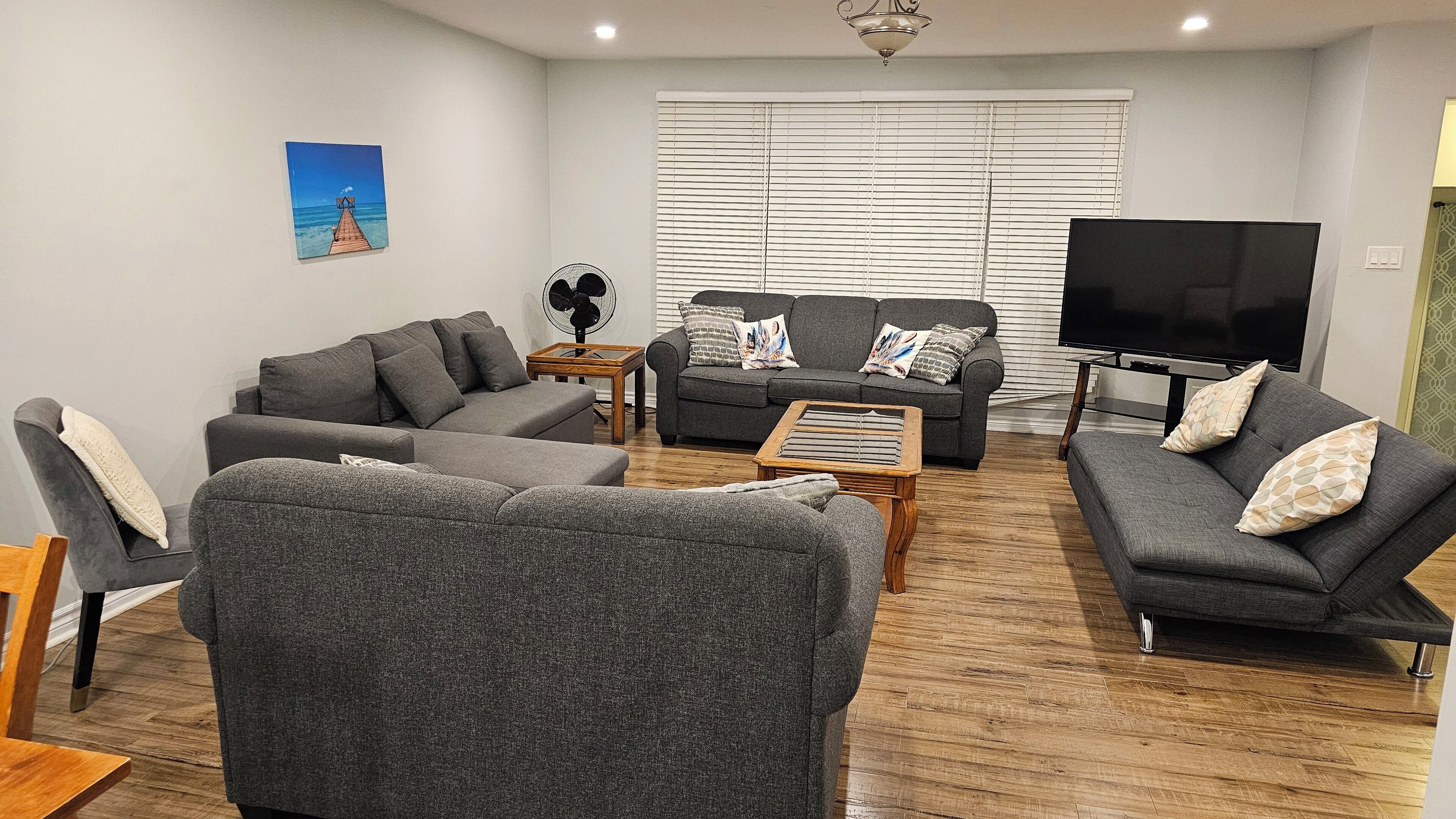A living room with grey sofas, a wooden coffee table, a TV, and a window with blinds.