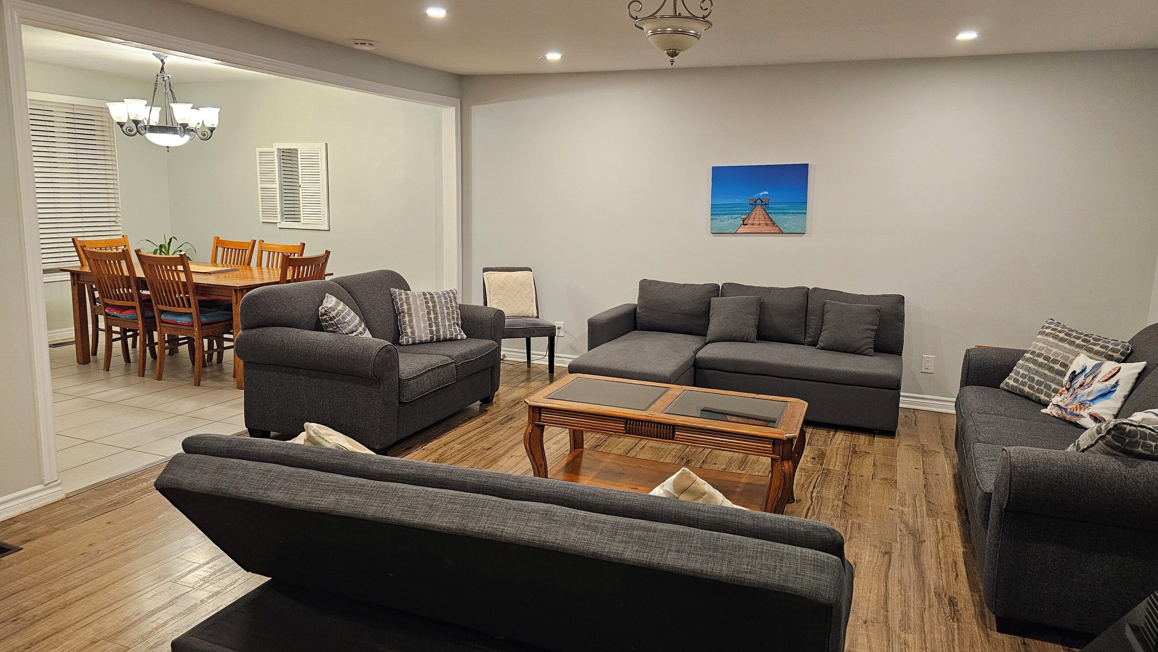 A modern living room with grey sofas, a wooden coffee table, and a dining area with wooden chairs and a table.