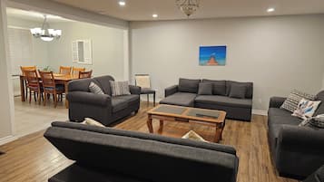 A modern living room with grey sofas, a wooden coffee table, and a dining area with wooden chairs and a table.