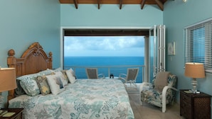 A bedroom with a bed, a chair, a nightstand, and a view of the ocean.