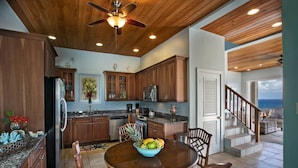 A kitchen with wooden cabinets, a stainless steel refrigerator, a dining table with chairs, and a ceiling fan.