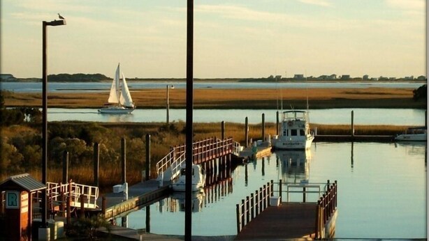 A marina with a dock, a sailboat, and a small building with a 'R' sign. - Rest, Relax & Enjoy Your Stunning Water Views in the Heart of Southport, NC! (Southport)