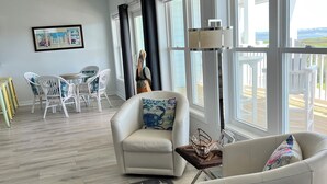 A spacious living area with a large window, a white armchair, a dining table with chairs, and a decorative rug. - Rest, Relax & Enjoy Your Stunning Water Views in the Heart of Southport, NC! (Southport)