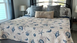 A bedroom with a bed, a nightstand, a lamp, and a window with curtains. - Rest, Relax & Enjoy Your Stunning Water Views in the Heart of Southport, NC! (Southport)