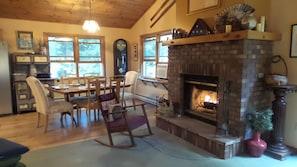 Cozy living room with a traditional fireplace, dining area, and large windows offering views of the surrounding landscape.