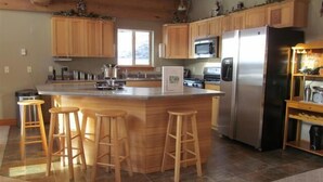 Une cuisine dotée de meubles en bois, d’un réfrigérateur en acier inoxydable, d’un four à micro-ondes et d’un grand îlot central avec des tabourets.