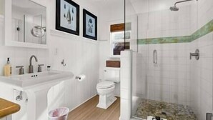 Uma casa de banho moderna com chuveiro de cabine de vidro, lavatório branco e sanita.