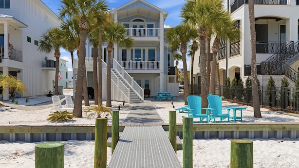 A beachfront property with a two-story building, a wooden deck, and a sandy walkway leading to a seating area with chairs. - Navarre Beach Southside bring your boat and jet skis huge private pier (Navarre)