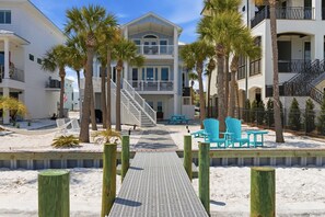 A beachfront property with a two-story building, a wooden deck, and a sandy walkway leading to a seating area with chairs. - Navarre Beach Southside bring your boat and jet skis huge private pier (Navarre)