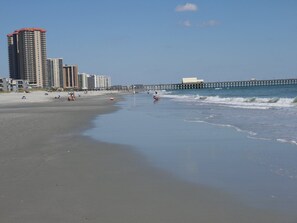 Een strand met een pier die het water in loopt, omringd door hoge gebouwen.