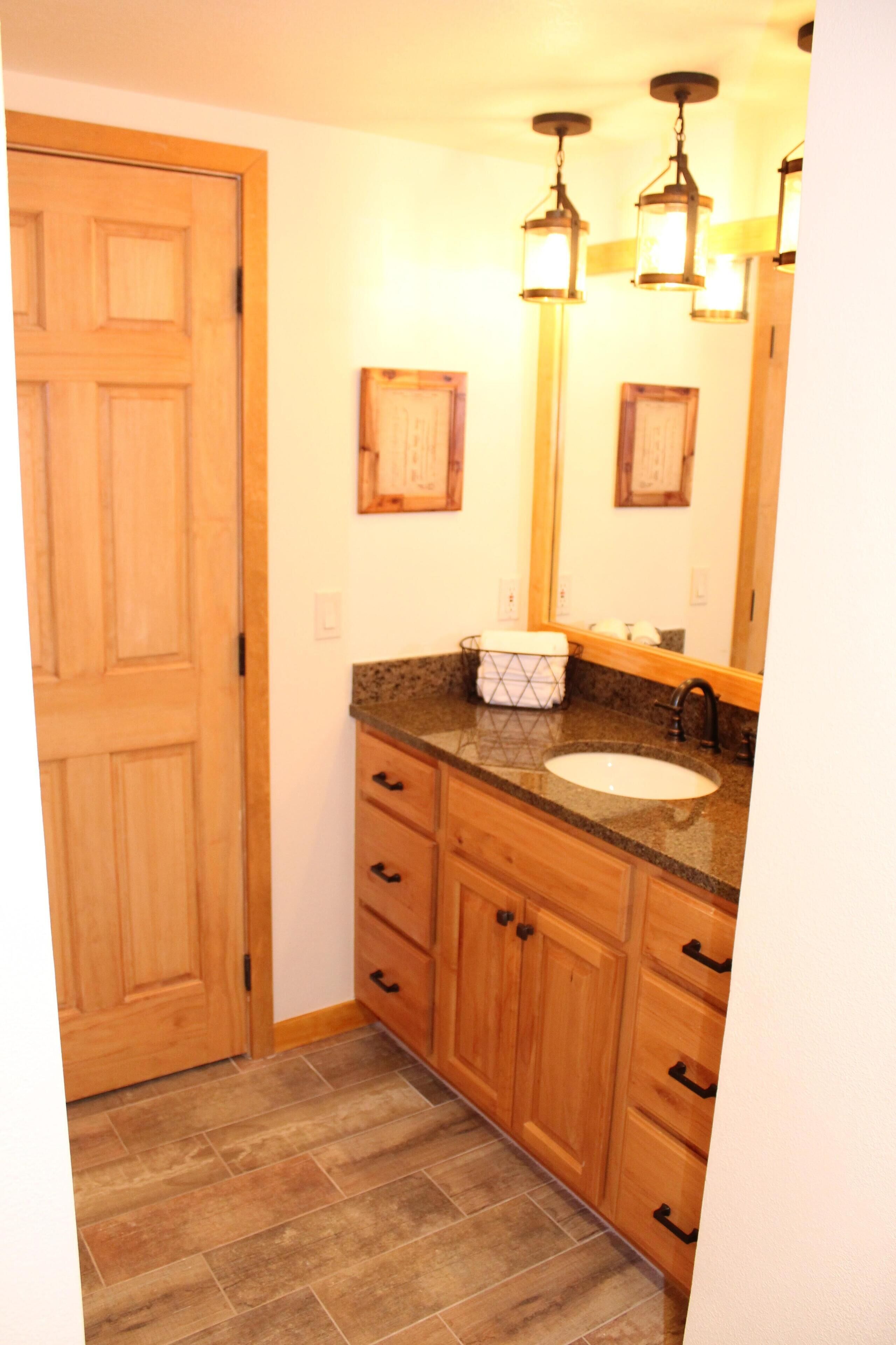 A bathroom with wooden cabinets, a granite countertop, a sink, and a mirror with wall-mounted lights.