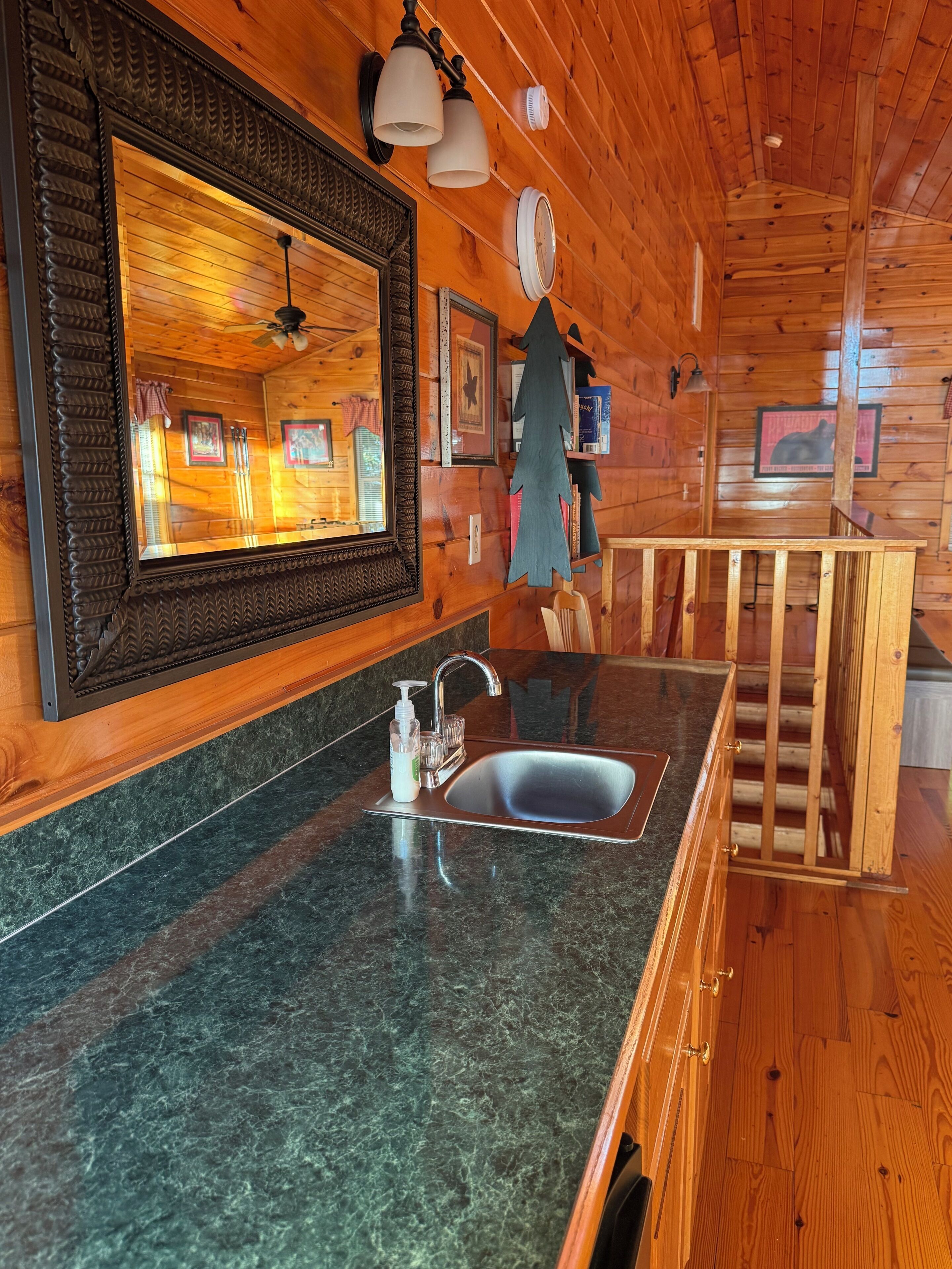 Un interno in legno con angolo cottura, caratterizzato da un piano di lavoro in granito, un lavello e uno specchio con modanature decorative.