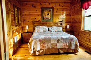 A wooden cabin bedroom with a bed, two bedside tables, a nightstand, and a window with curtains. - 6 BD 6 BATH ALL Ensuite cabin. Come make memories for a lifetime! (Sevierville)