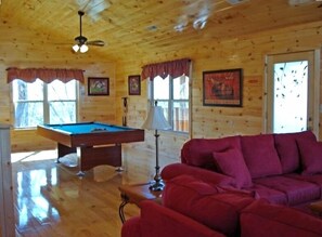 A wooden cabin interior with a pool table, red sofa, and framed pictures on the walls. - 6 BD 6 BATH ALL Ensuite cabin. Come and make memories for a lifetime! (Sevierville)