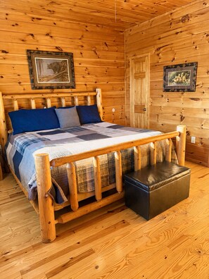A wooden cabin room with a bed, a bench, and two framed pictures on the walls. - 6 BD 6 BATH ALL Ensuite cabin. Come and make memories for a lifetime! (Sevierville)