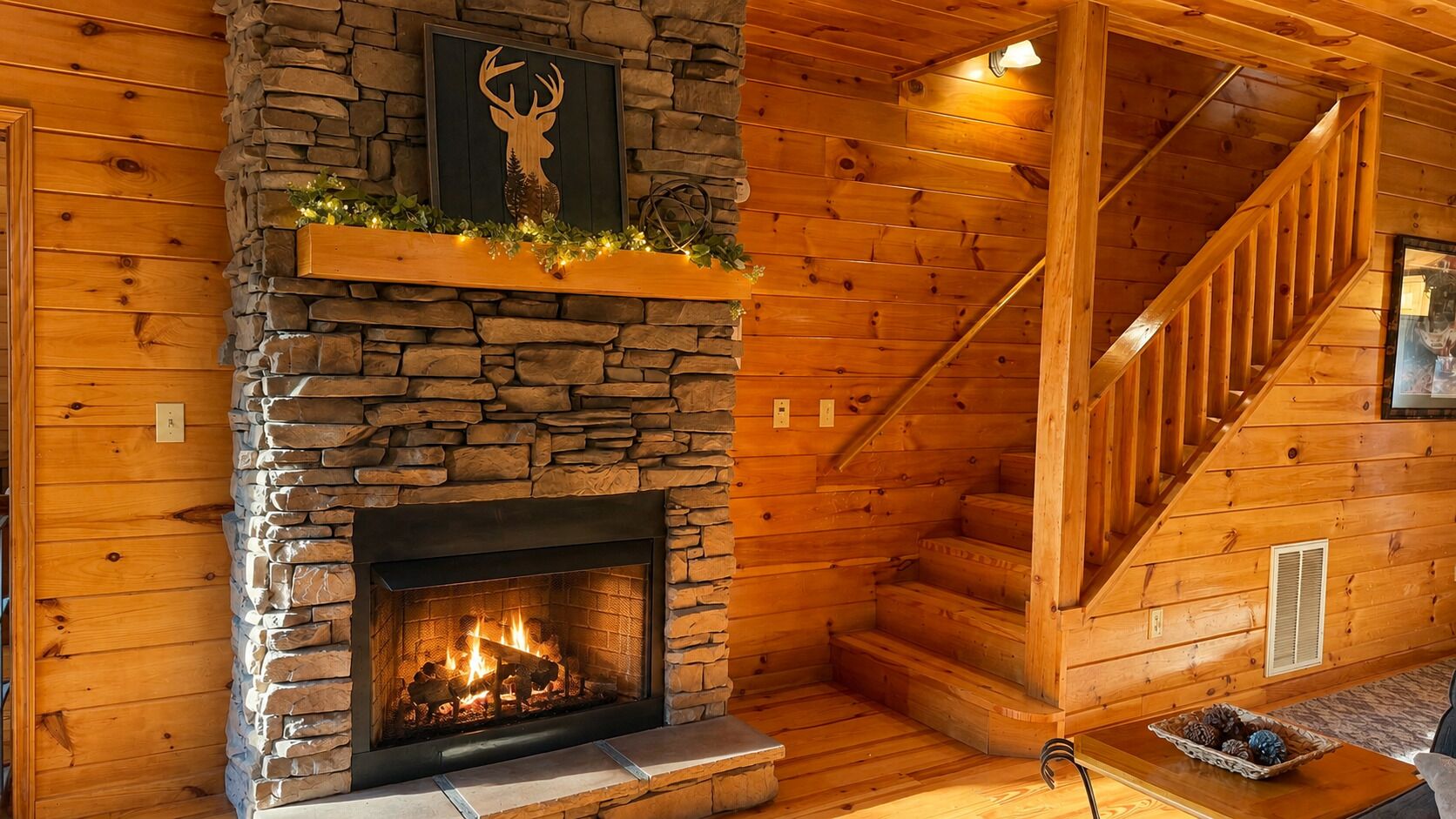 Un intérieur en bois avec une cheminée en pierre, une tête de cerf décorative et un escalier.