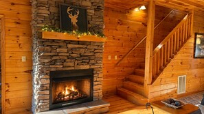 A wooden interior with a stone fireplace, a deer head decoration, and a staircase.