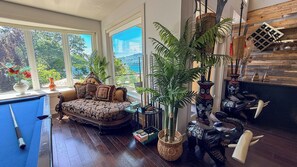 A room with a large window, a sofa, a blue chair, a potted plant, and decorative vases.