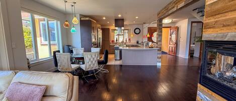 A spacious living area with a sofa, dining table, and chairs, a kitchen with modern appliances, and a fireplace.