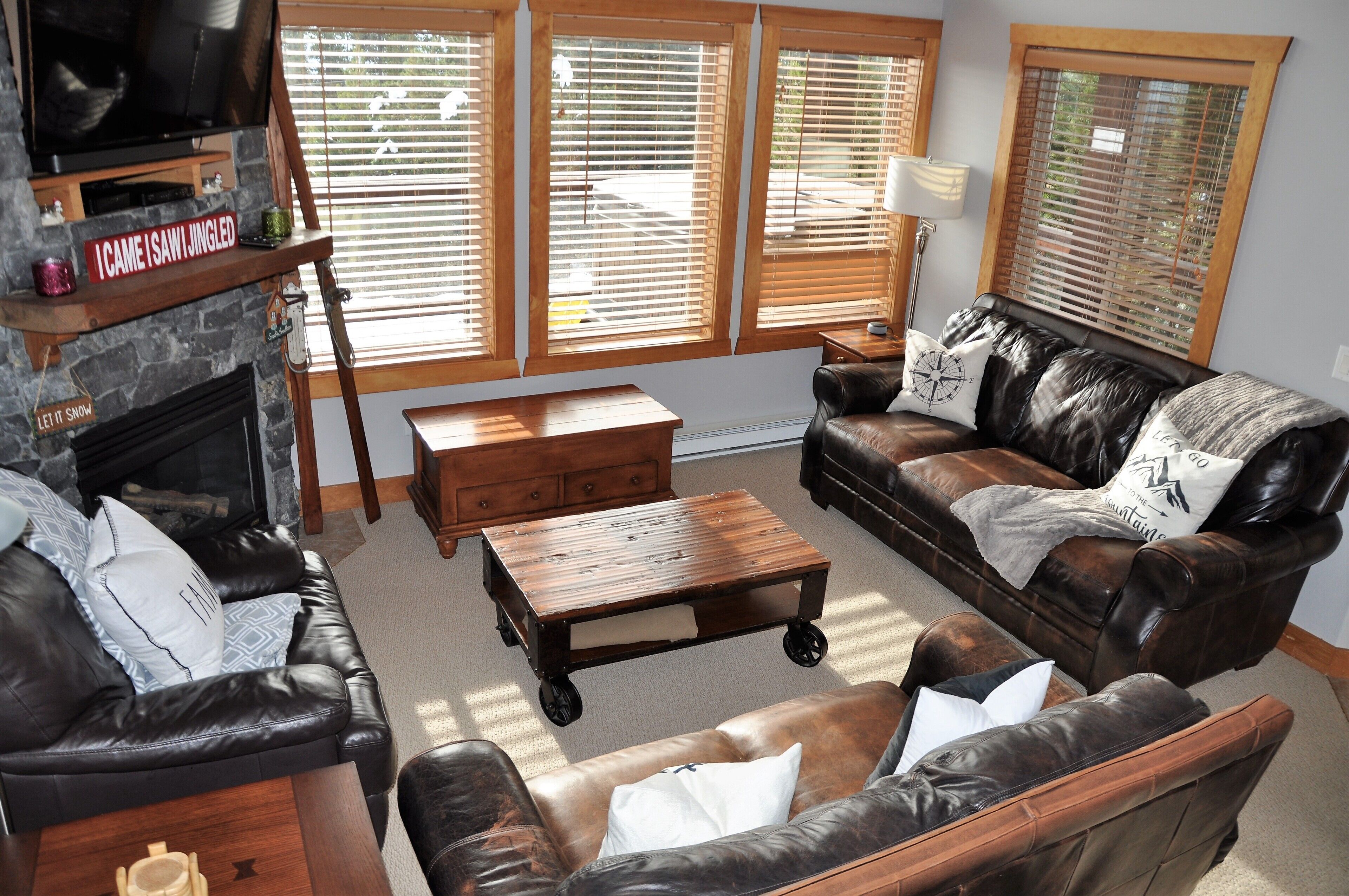 A living room with a fireplace, leather sofas, a coffee table, and large windows with blinds.