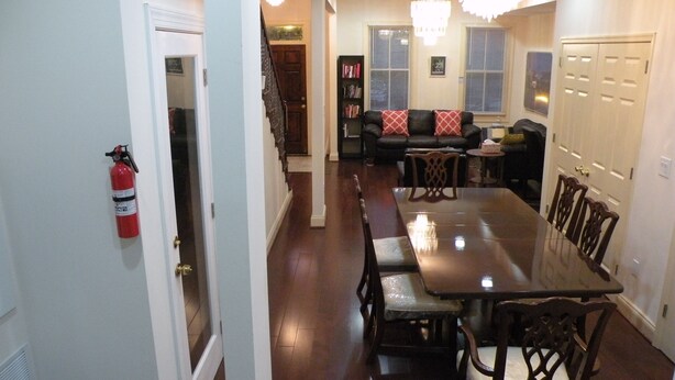 A dining area with a long table and chairs, a fire extinguisher on the wall, a sofa with cushions, and a bookshelf. - 5 BR 4 BA New House- 1 Block to Library of Congress -Free Parking Permit (Washington)
