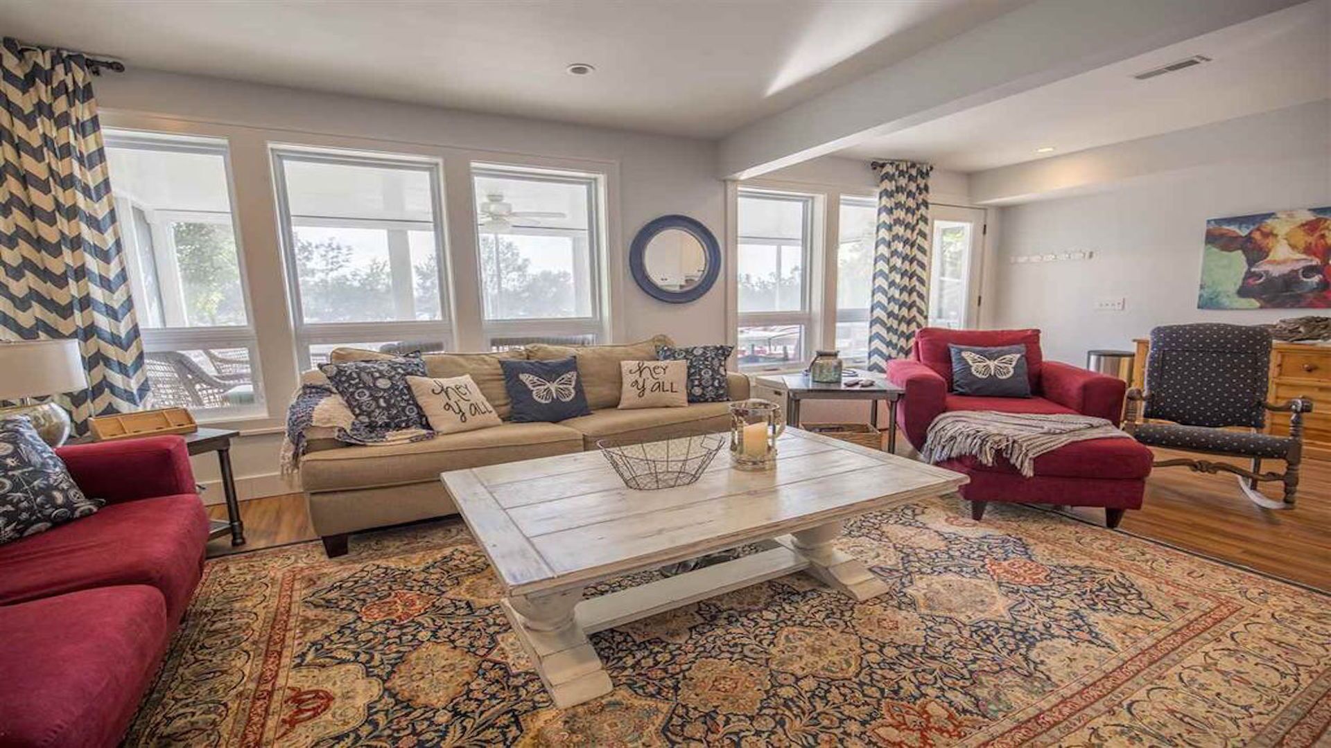 A spacious living room with a beige sofa, red armchairs, and a patterned rug.
