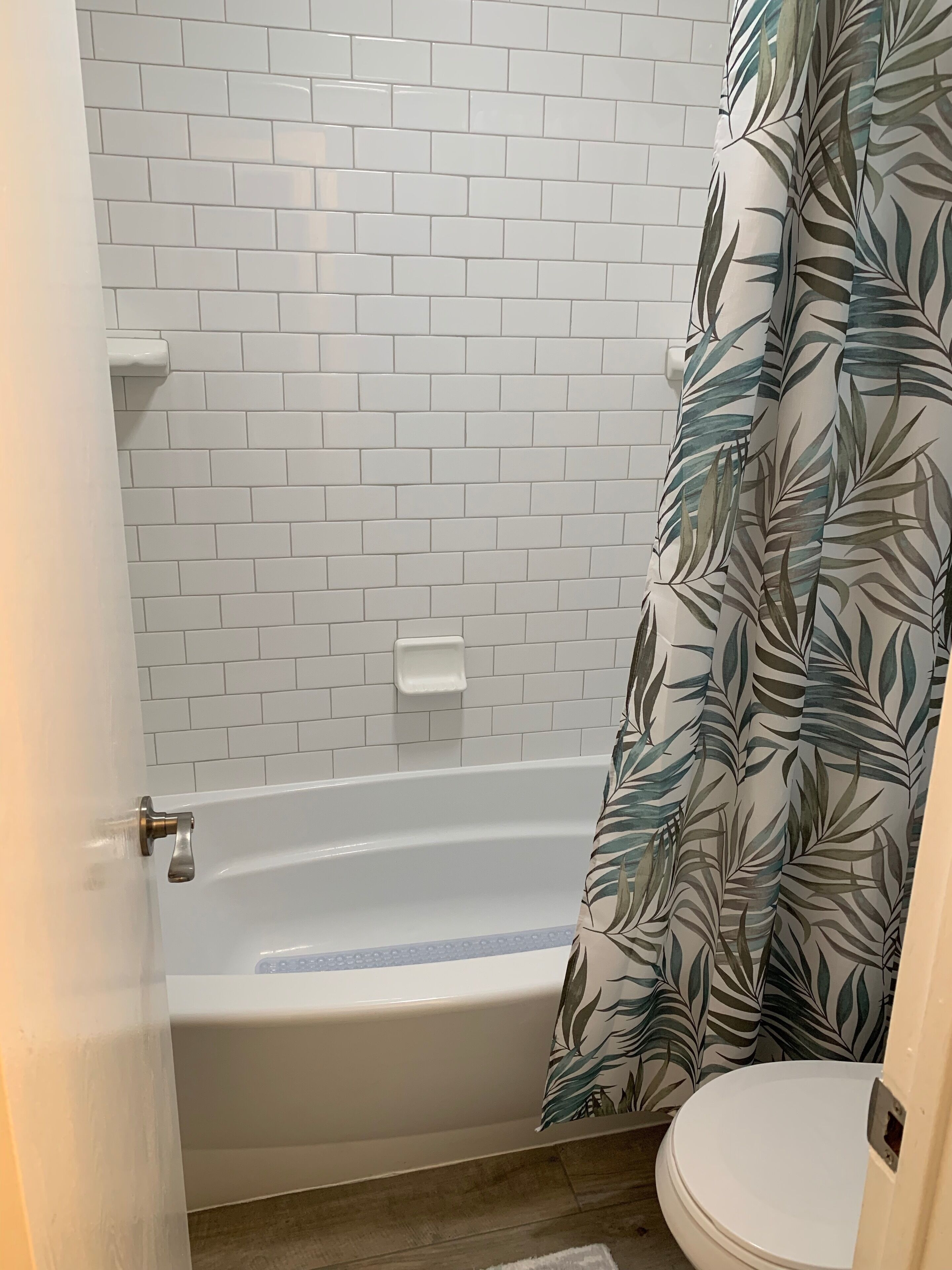 Une salle de bain avec un mur recouvert de carreaux blancs, une baignoire blanche et des toilettes.