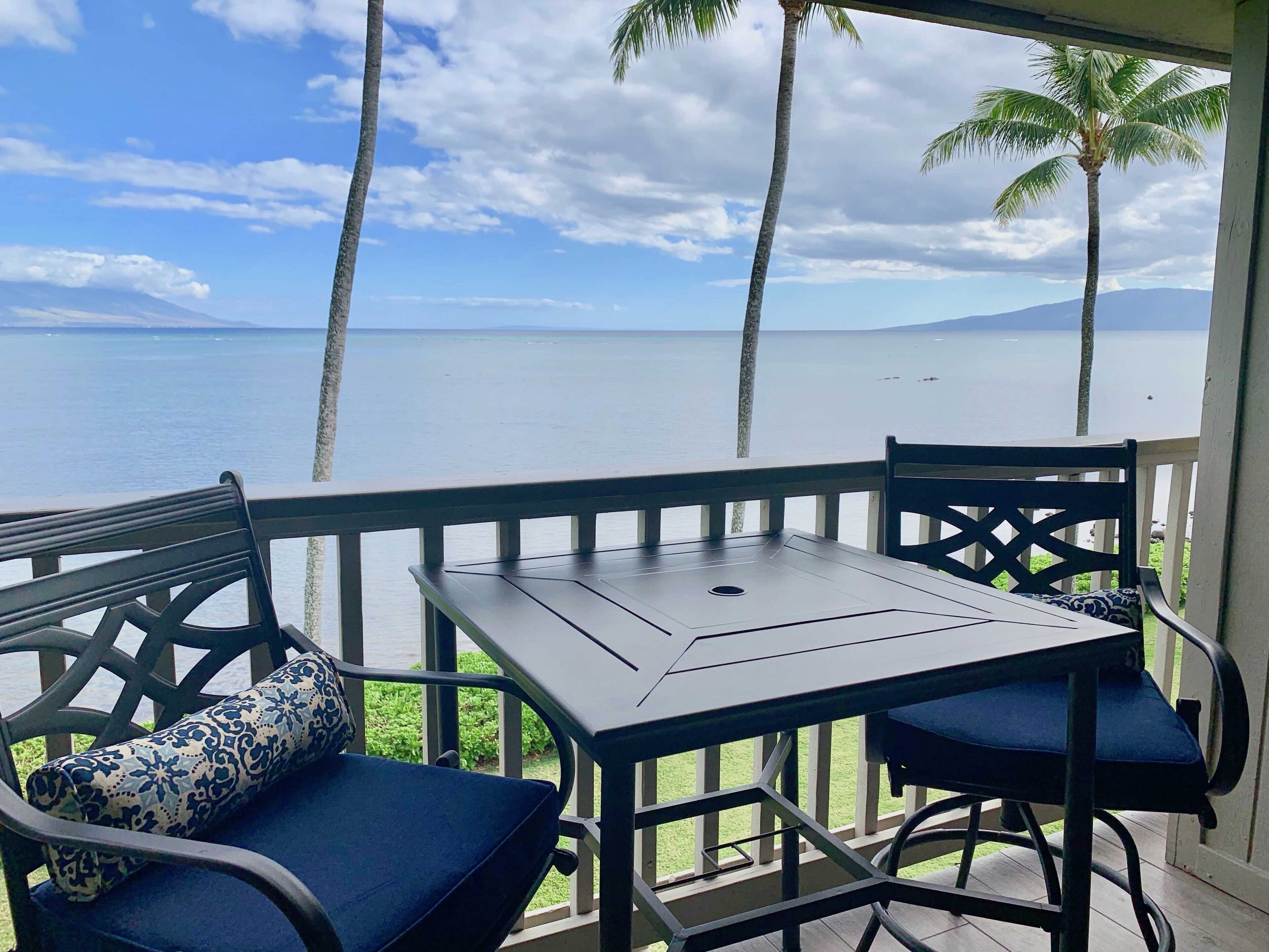 A balcony with a table and chairs, overlooking a body of water and palm trees.