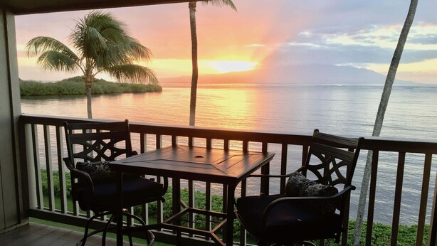 A balcony with a table and chairs overlooking a sunset over the water.
