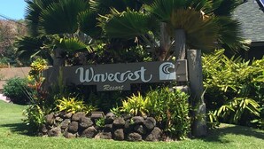 A sign for Wavecrest Resort surrounded by lush greenery and a stone wall.