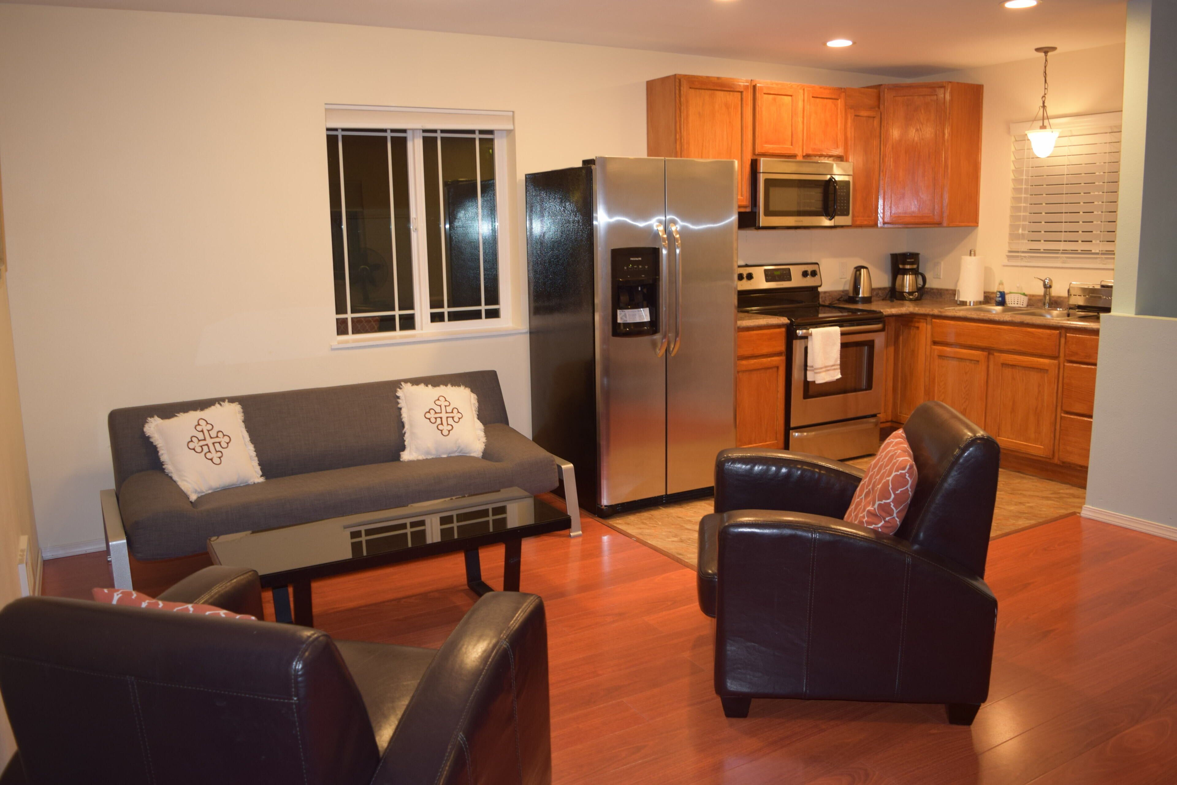 A compact living space with a sofa, two chairs, a refrigerator, a microwave, and a kitchenette.