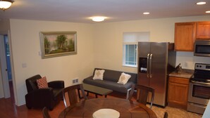 A modern kitchen with a refrigerator, oven, and microwave. There is a dining area with a round table and chairs. A sofa and a chair are also visible. - Park like setting, brand new built, 1 bedroom ADU (Shoreline)