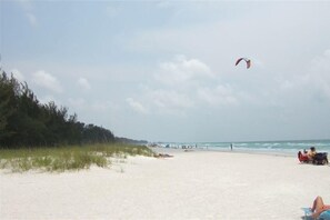 A beach with a clear sky, a kite flying, and people relaxing on the sand. - Gorgeous Home July specials check it out, heated pool and spa, elevator (Holmes Beach)