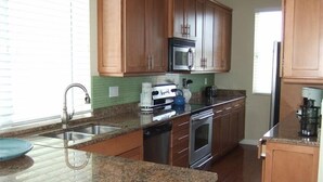 Una cocina con armarios de madera, electrodomésticos de acero inoxidable, encimeras de granito y un ventanal que proporciona luz natural.