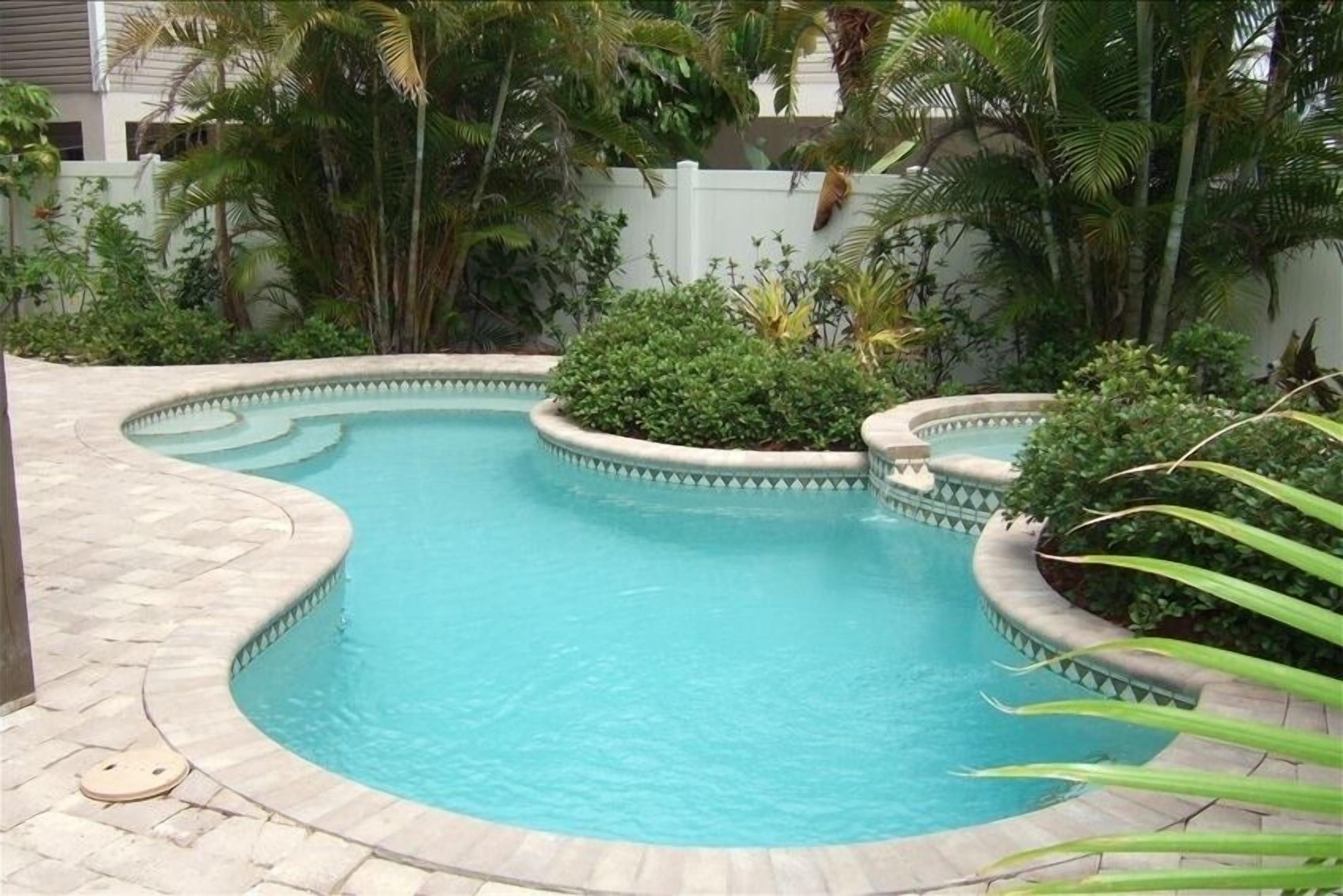 Ein gewundener Pool mit Steinrand, umgeben von üppiger Vegetation und einem weißen Zaun.