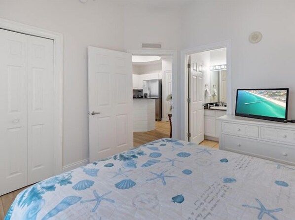 A bedroom with a bed, a TV, and a view of a kitchen and bathroom through an open door. - 2301 East Calypso Penthouse Corner Unit. Views for Miles, All new in 2025! (Panama City Beach)