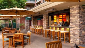 An outdoor patio area with wooden tables and chairs, stone pillars, and a bar with illuminated shelves. - Confirmed Reservation - March 13–20, 2027 - 1BR Premium Villa - Instant Book (Scottsdale)