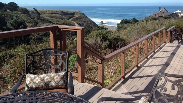 Um deck de madeira com guarda-corpo, com vista para a paisagem costeira.