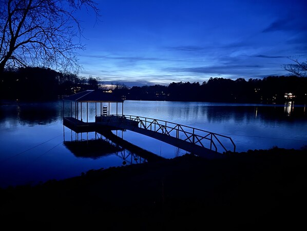 A calm lake at dusk with a dock and a small building, surrounded by trees and distant lights. - Pristine views from Lakefront Home  (Seneca)