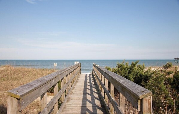 A wooden boardwalk leading to a beach with a clear sky.