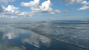 A beach with waves approaching the shore under a partly cloudy sky.