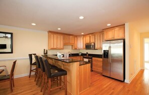 A kitchen with wooden cabinets, a stainless steel refrigerator, and a bar area with stools.