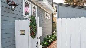 A white wooden gate with a holiday wreath and a plaque, leading to a house with grey siding and a brick pathway. - Hagan's Hideaway (Encinitas)