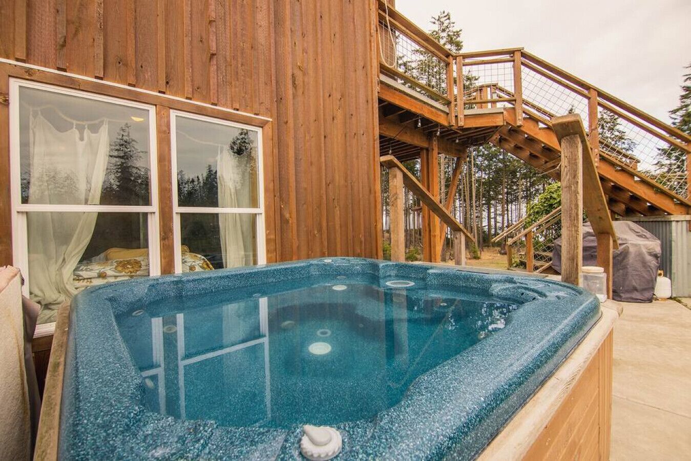 Une cabane en bois avec un jacuzzi, un escalier et une fenêtre avec des rideaux.