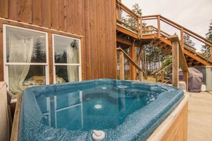 Una cabaña de madera con jacuzzi, una escalera y una ventana con cortinas.