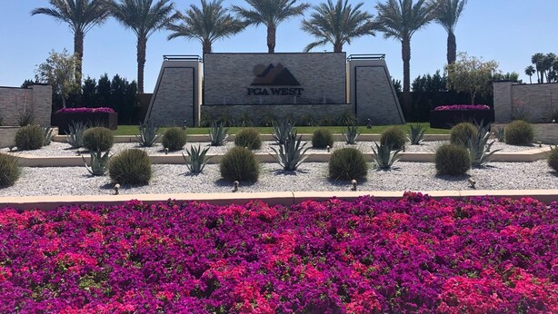 A sign for PGA WEST with a landscaped garden in front, including palm trees and purple flowers. - Charming and Contemporary 5 Star PGA West Condo Stadium on11th Tee Box Lic100888 (La Quinta)