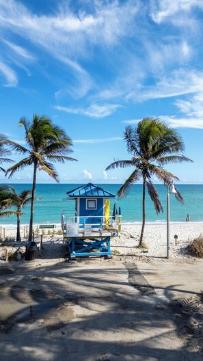 Une tour de surveillance sur une plage, avec des palmiers et un ciel bleu dégagé.